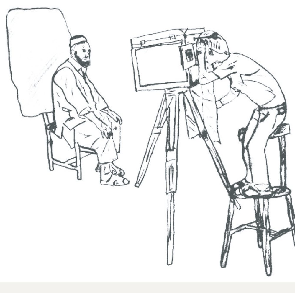 The photographer works from a stool, head bent to the box.