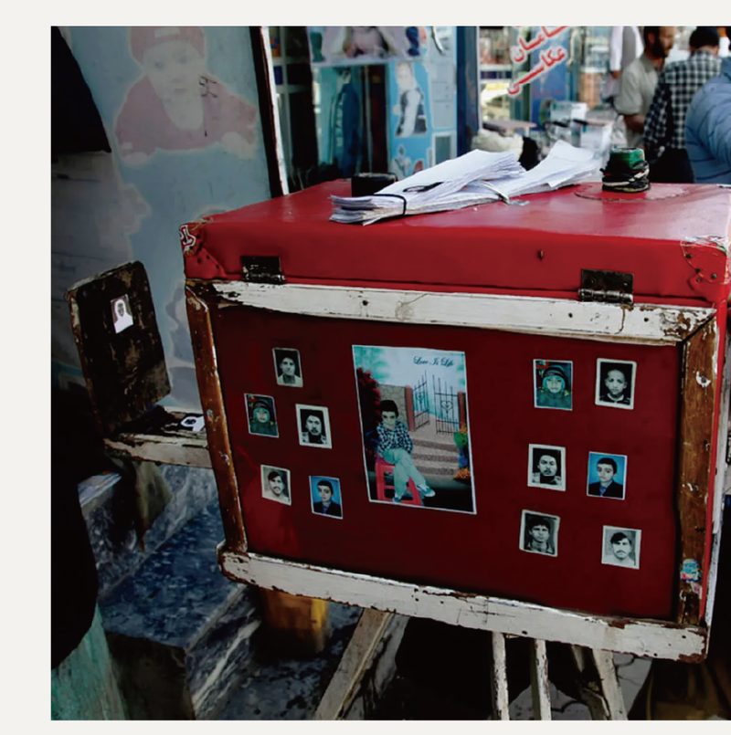 A street photographer’s box camera, Kabul — hand-painted, tripod-mounted, sample portraits pinned to its face.