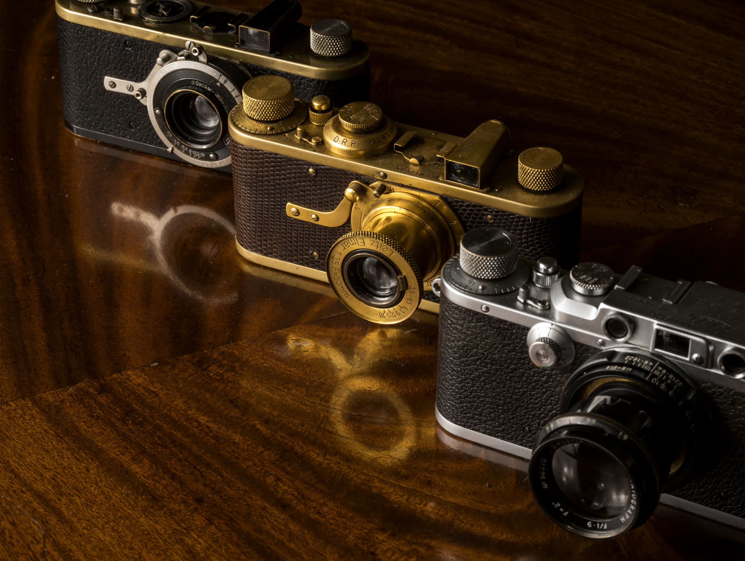 Three early Leica cameras on mahogany